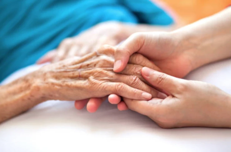 A younger person gently holding an older person’s hands